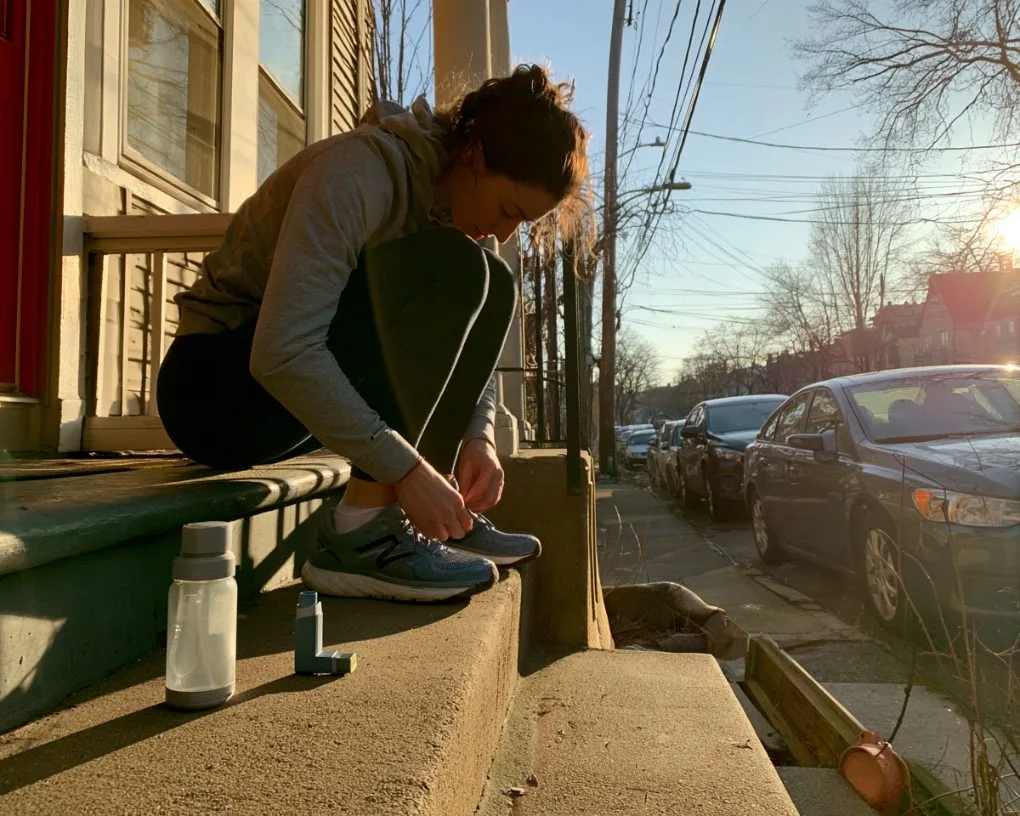 Woman lacing running shoes on a front step, inhaler and water bottle beside her
